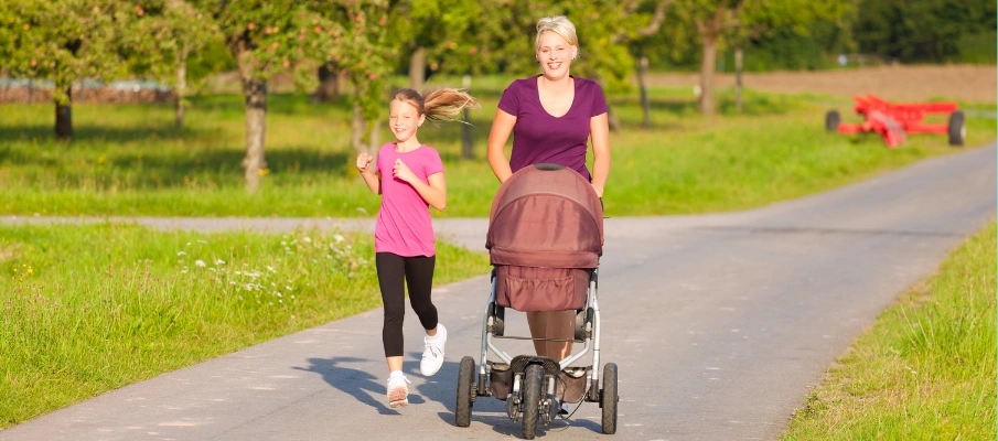 Madre e hija paseando a un bebe en una silla de paseo en el parque